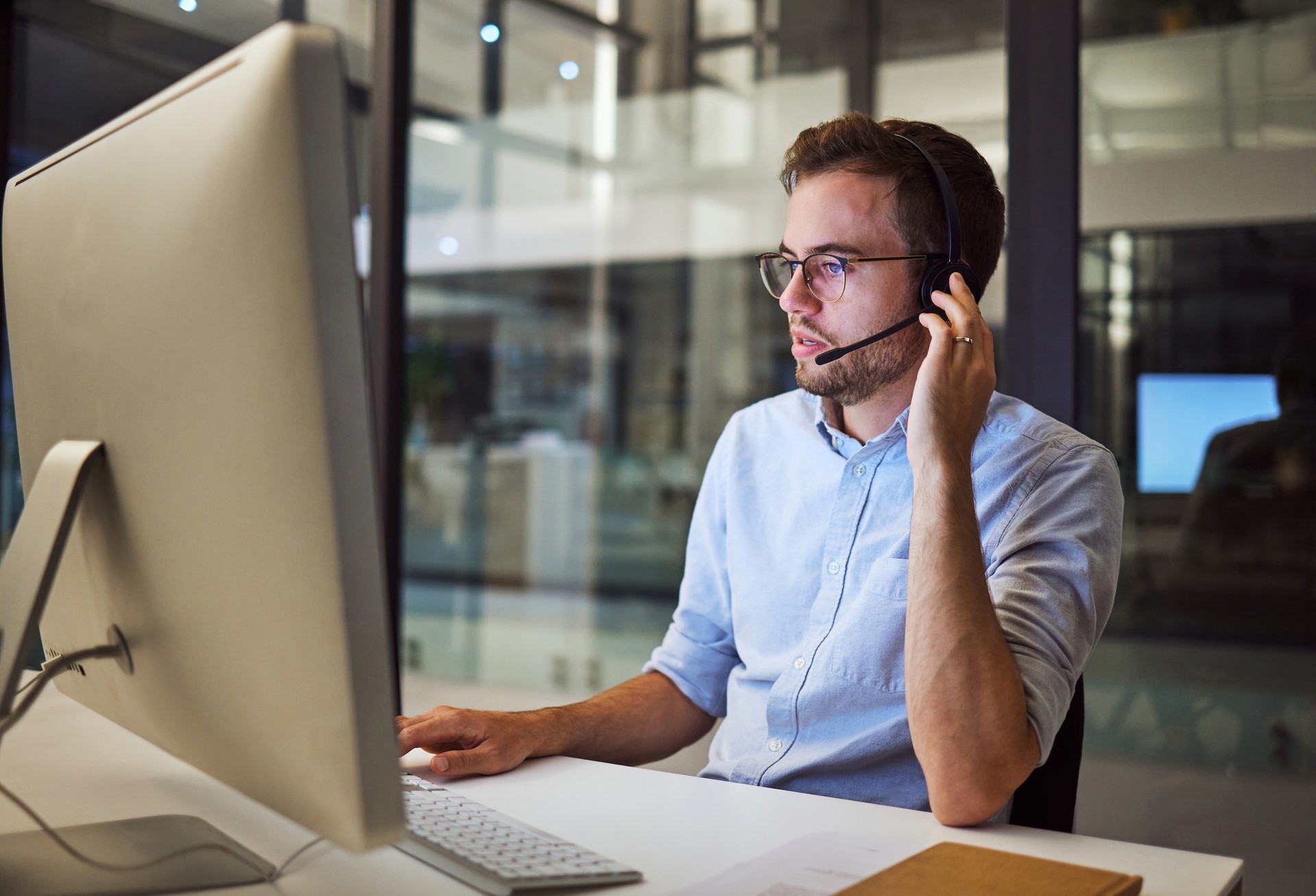 Telemarketing, man and employee in call center with headphones at desk. Worker or consultant at table on computer talking to client, checking information or consulting customer with technical support